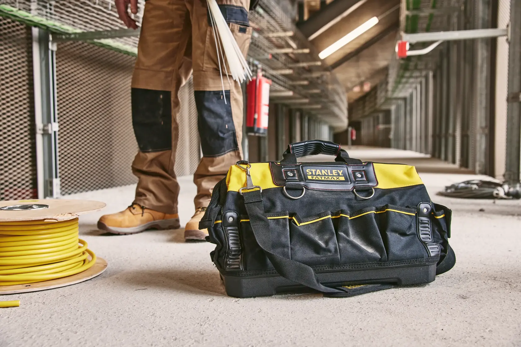 STANLEY 1-93-950 tool bag in black and yellow with handles, shown on a jobsite floor beside cable reel.