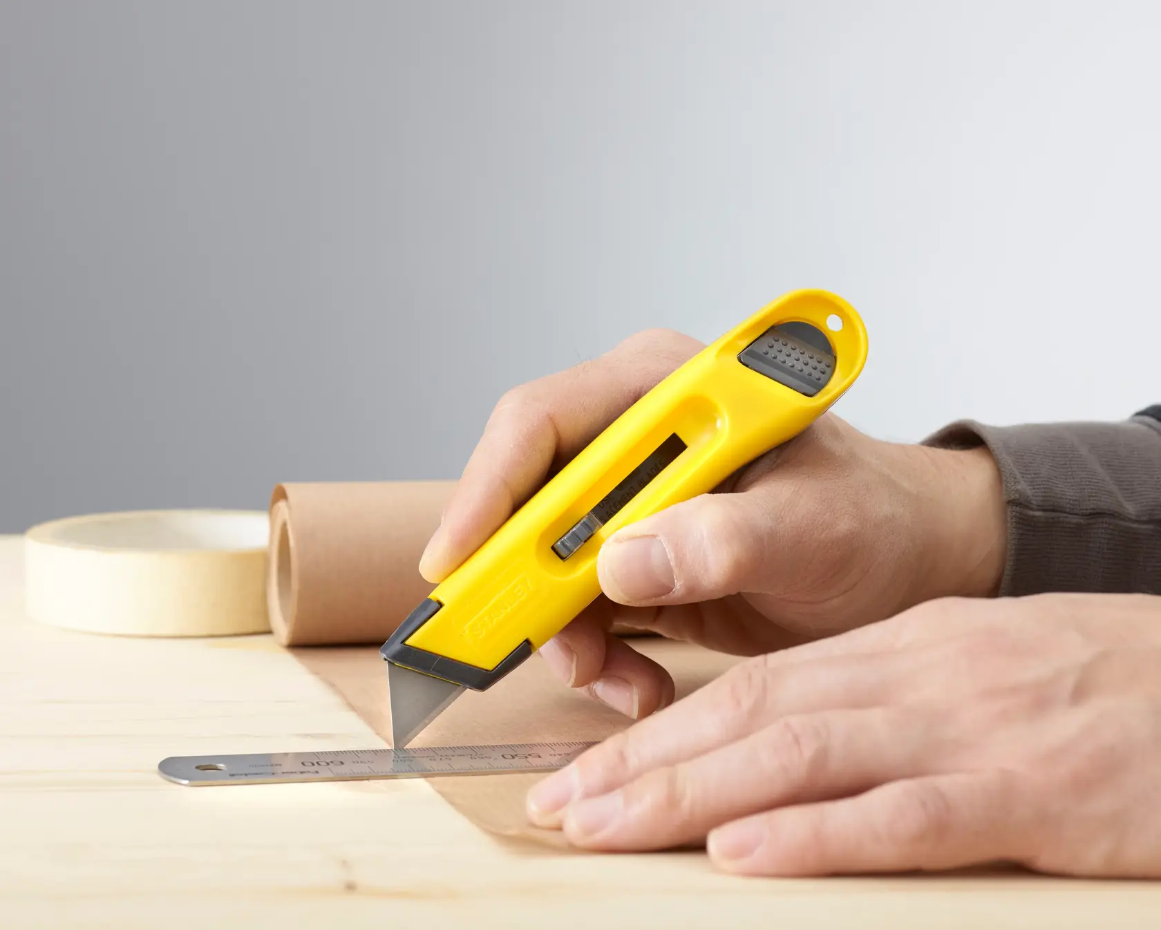 STANLEY 0-10-088 utility knife with yellow handle cutting paper alongside a metal ruler on a wooden table.