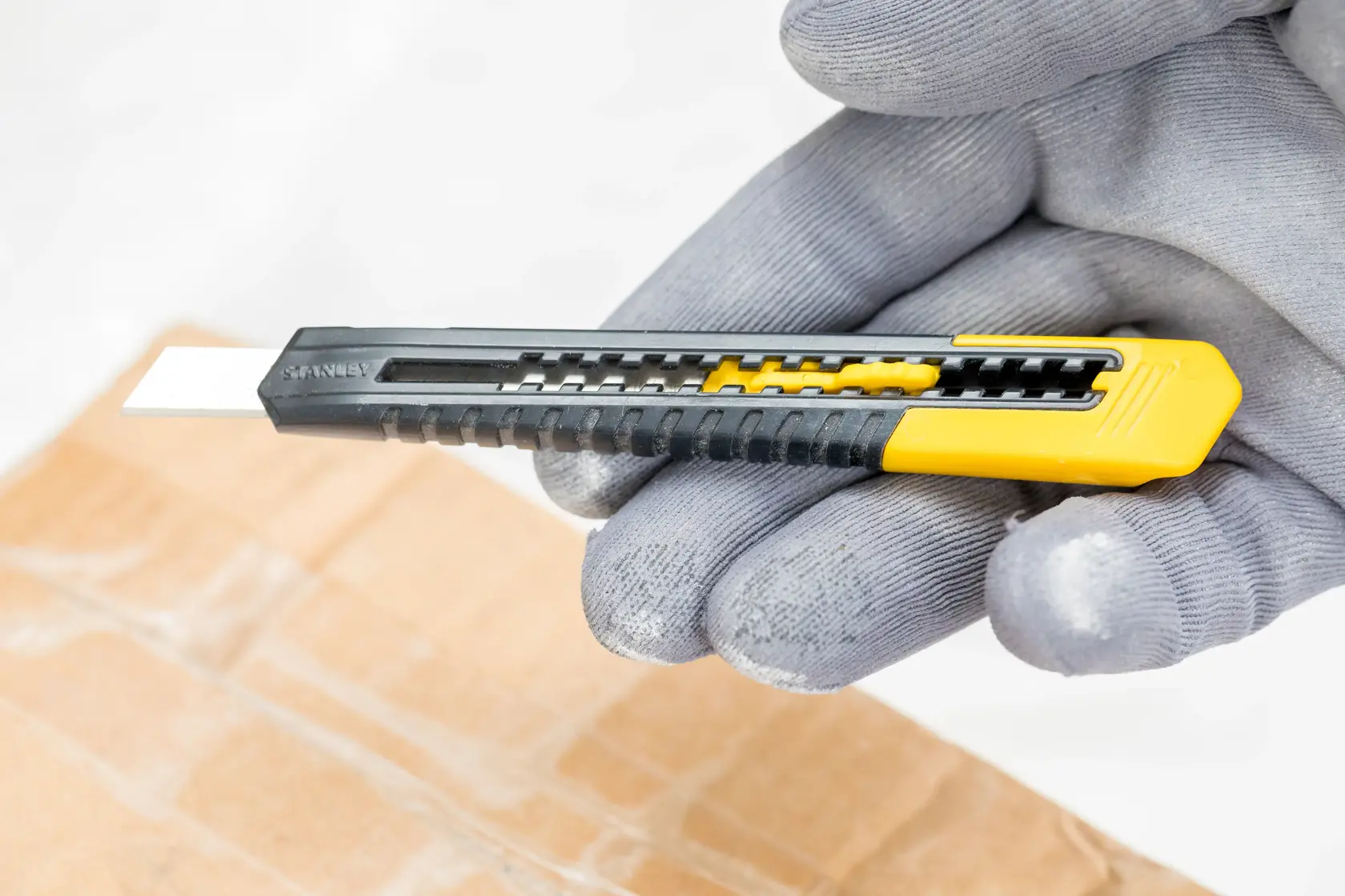 STANLEY 0-10-150 utility knife in black and yellow, held with a glove above cardboard.