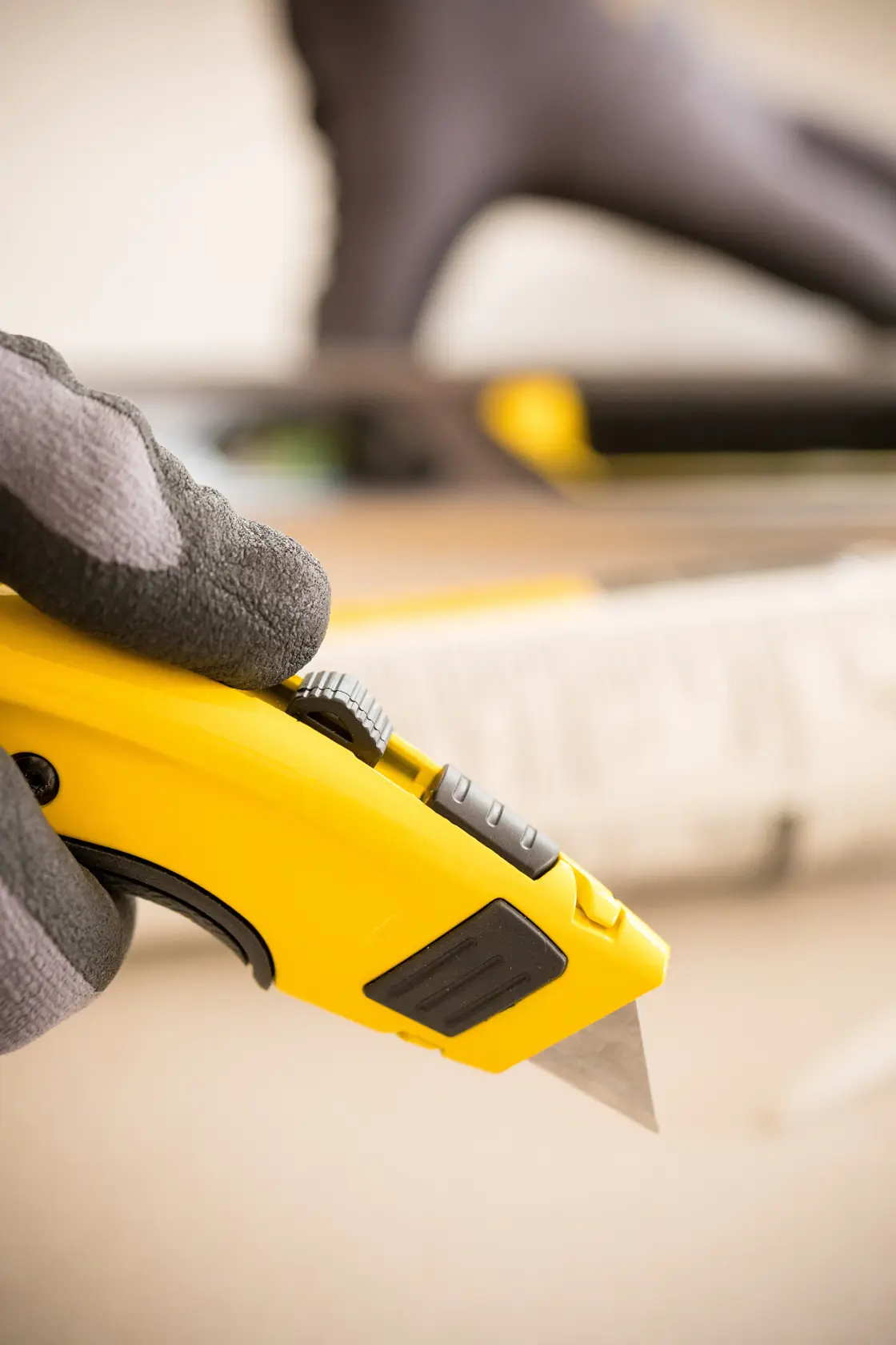 Photo of STANLEY 0-10-778 utility knife held in gloved hand, close-up view showing yellow body and exposed blade.