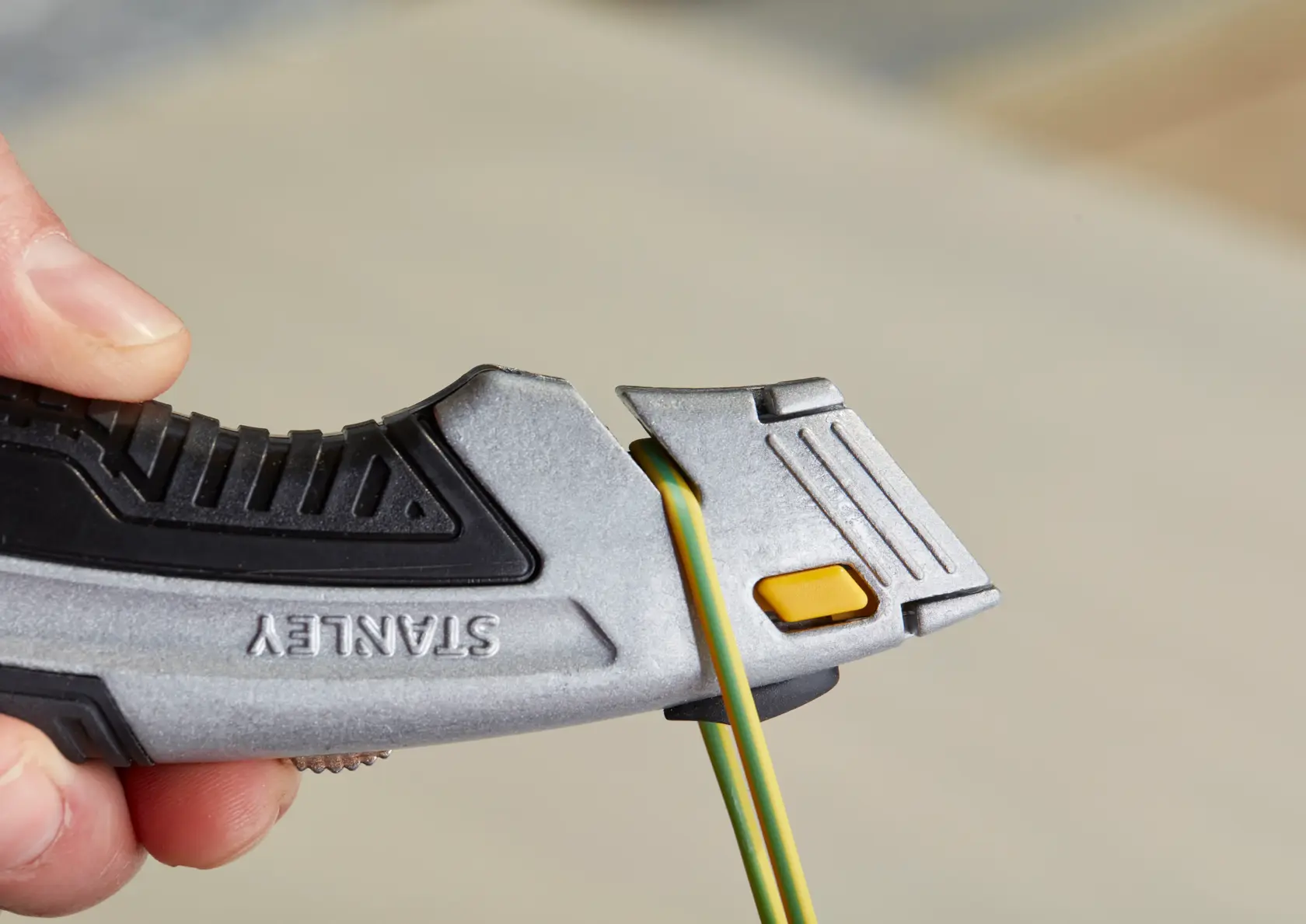 STANLEY 0-10-788 utility knife close-up, silver and black with yellow button, cutting green and yellow wire.