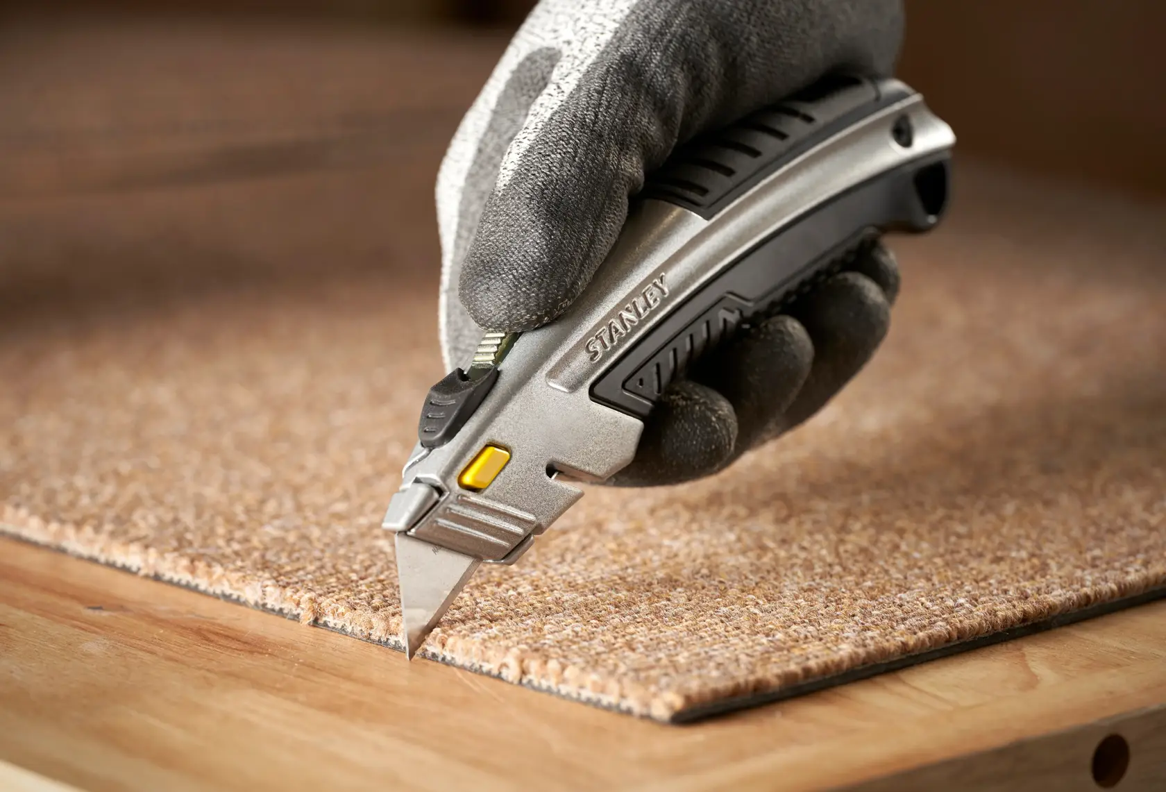 Photo of STANLEY 0-10-788 utility knife cutting carpet, held by gloved hand.
