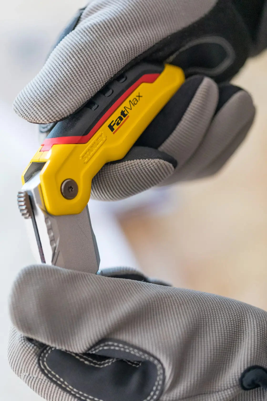 Photo of STANLEY 0-10-825 folding utility knife held in gloved hands, yellow and black handle visible.