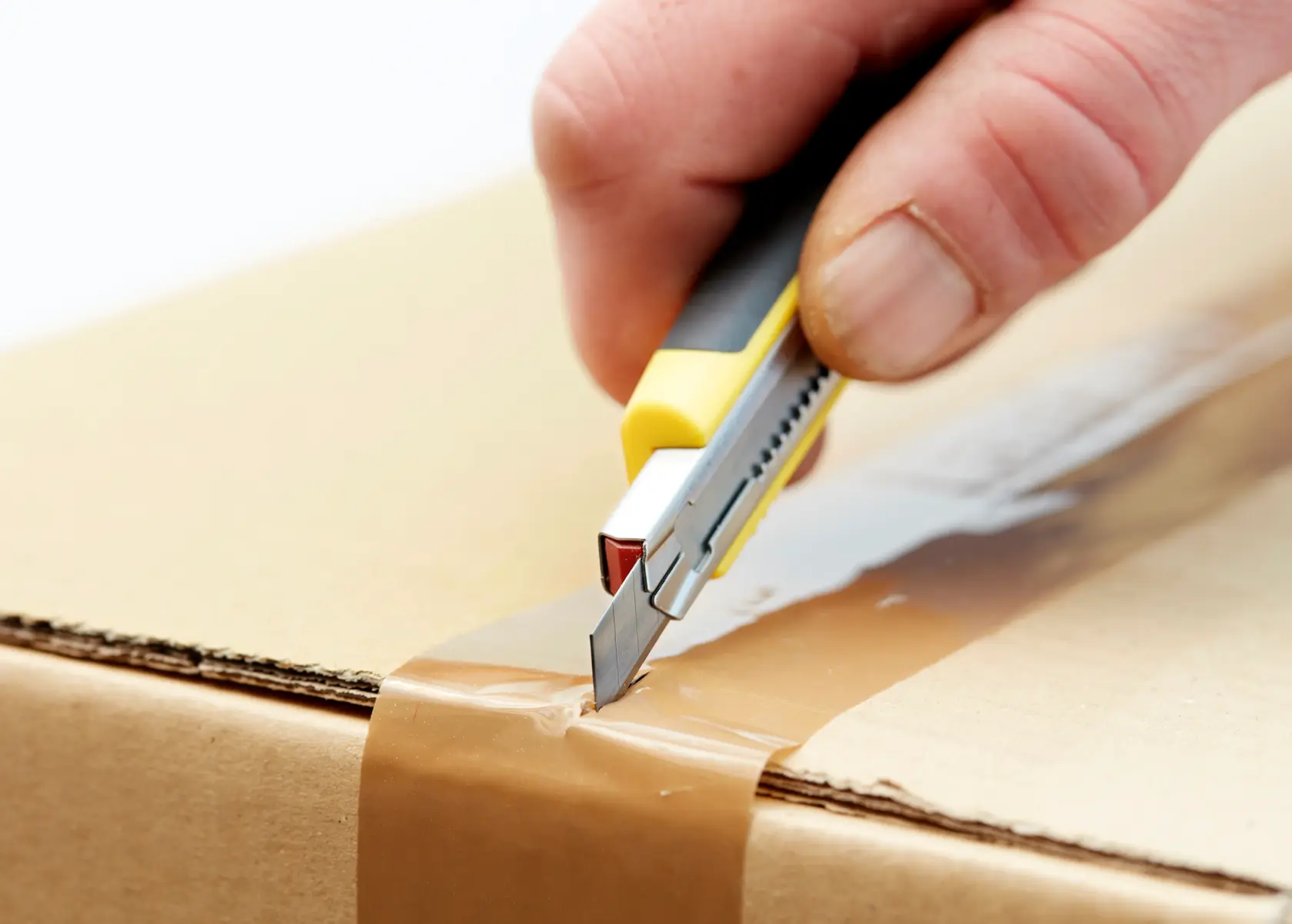 STANLEY 0-11-300 utility knife cutting brown tape on cardboard box, close-up photography.