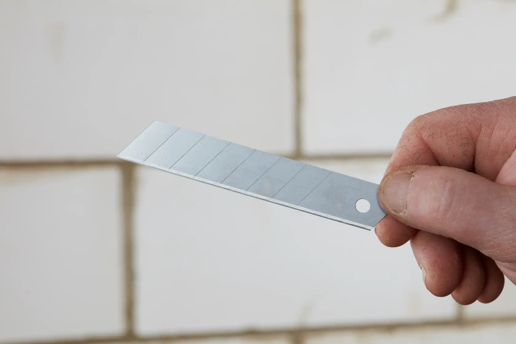 Photo of STANLEY 0-11-301 snap-off utility knife blade held in hand, silver with scored sections.