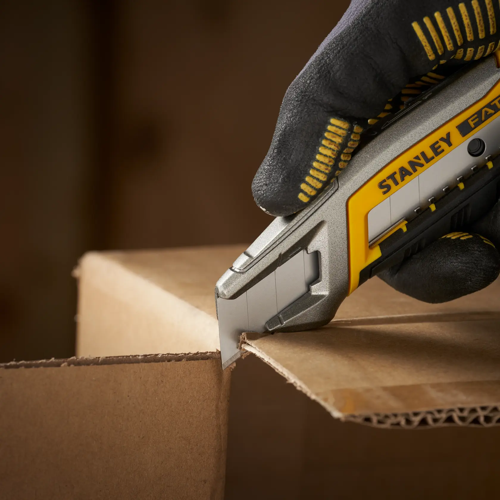 Photo of STANLEY 0-11-301 utility knife cutting cardboard, close-up view with gloved hand.