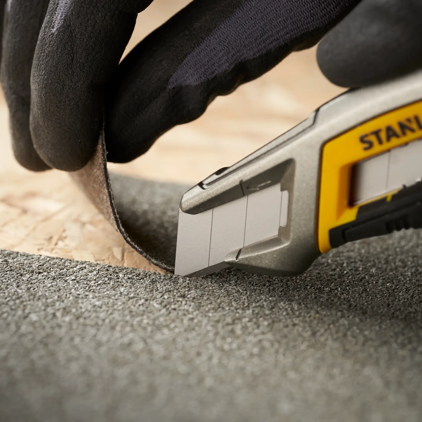 Photo of STANLEY 0-11-301 utility knife cutting abrasive material, close-up, gloved hand holding material.