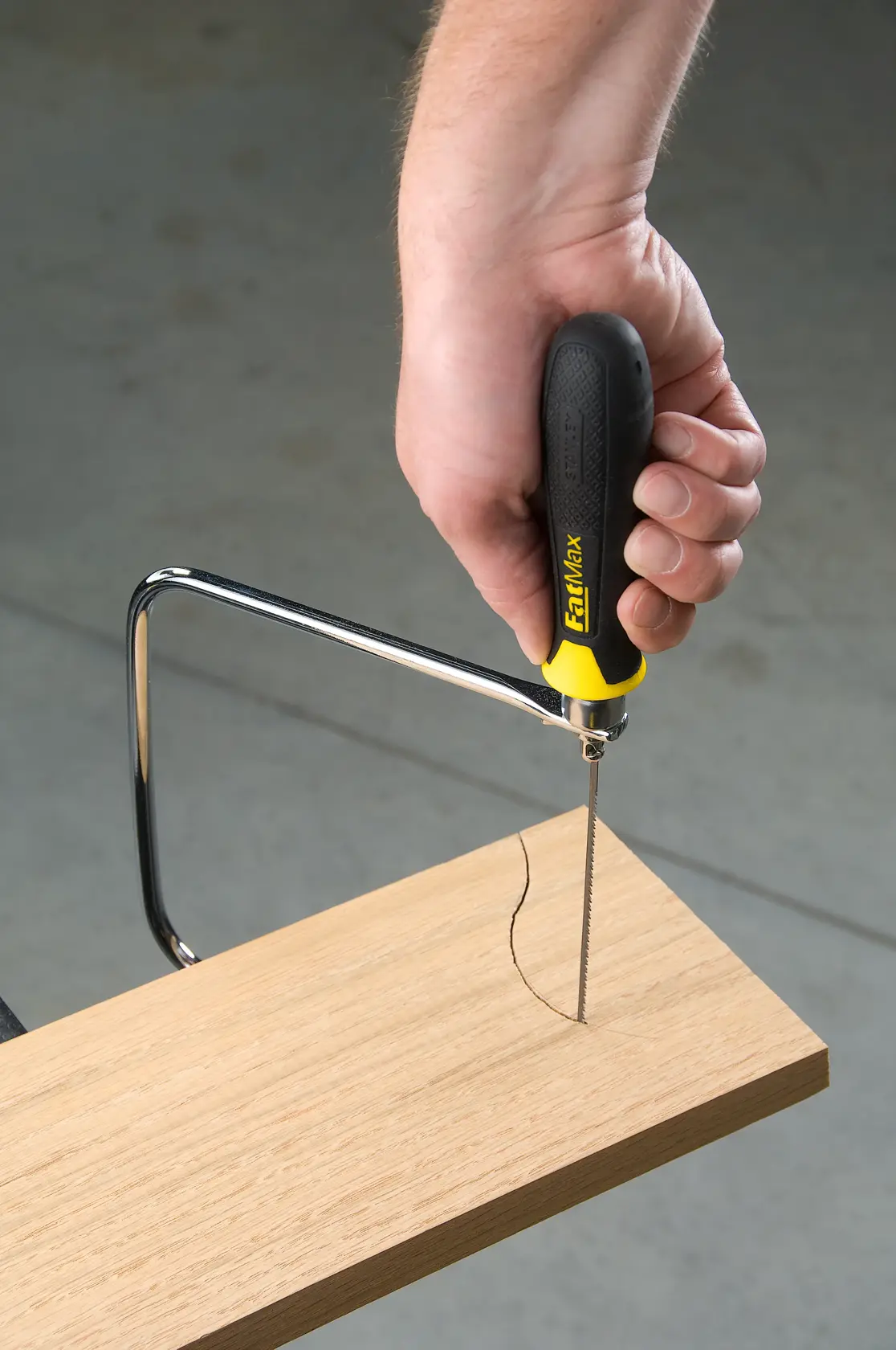STANLEY 0-15-106 coping saw with black and yellow handle cutting a curved line in a wooden board, close-up.