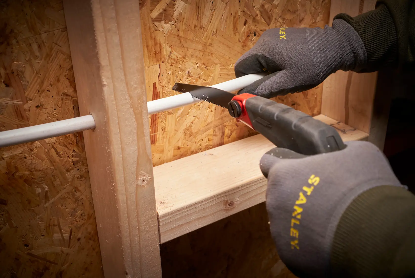 STANLEY 0-20-108 hand saw cutting white pipe, user wears Stanley gloves, photo at close angle.