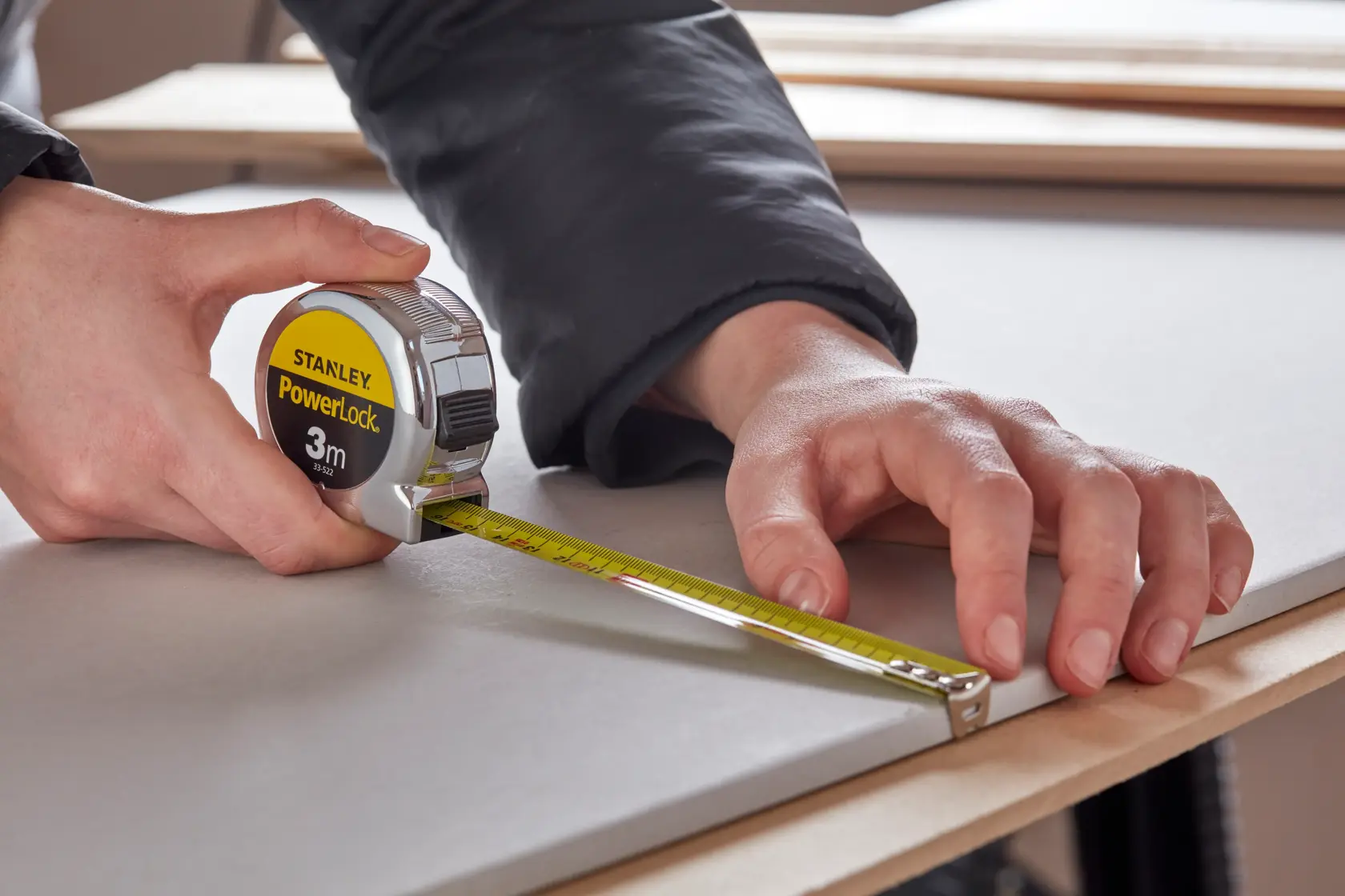 STANLEY 0-33-522 tape measure held by hand, measuring board surface, close-up photography.