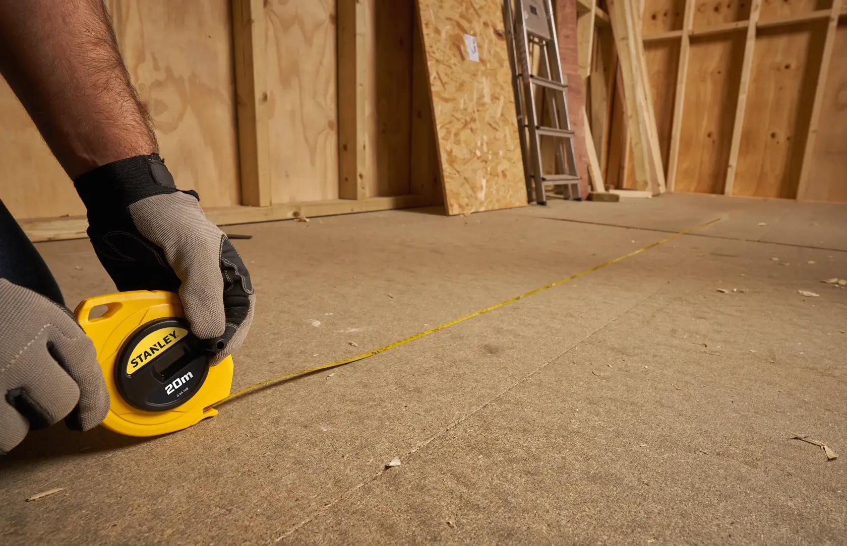 Stanley 0-34-105 measuring tape photography, yellow casing, extended on floor in construction setting.
