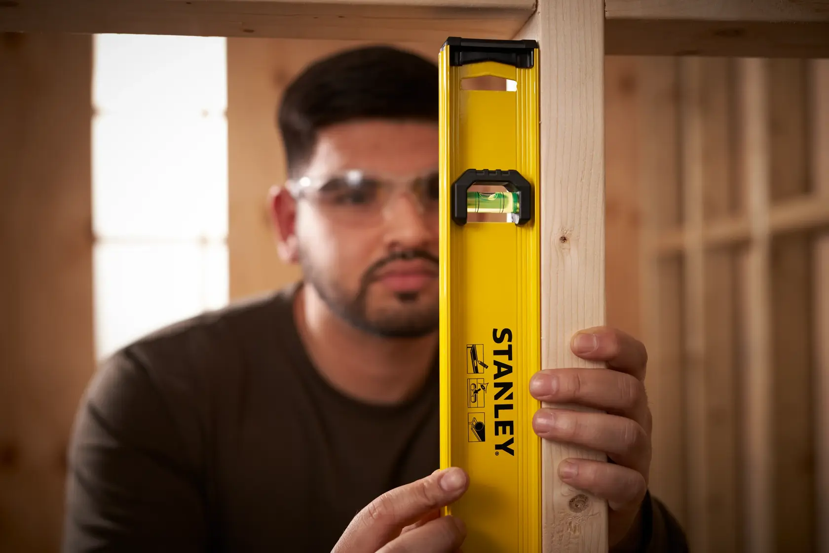 Stanley 0-42-074 yellow spirit level held vertically against wooden beam in workshop.