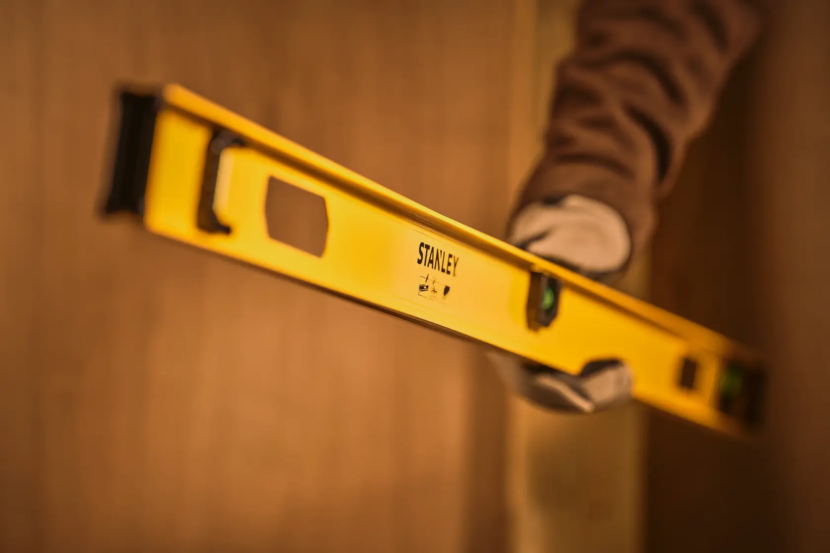 Stanley 0-42-076 yellow spirit level held by gloved hand in construction context, side angle.