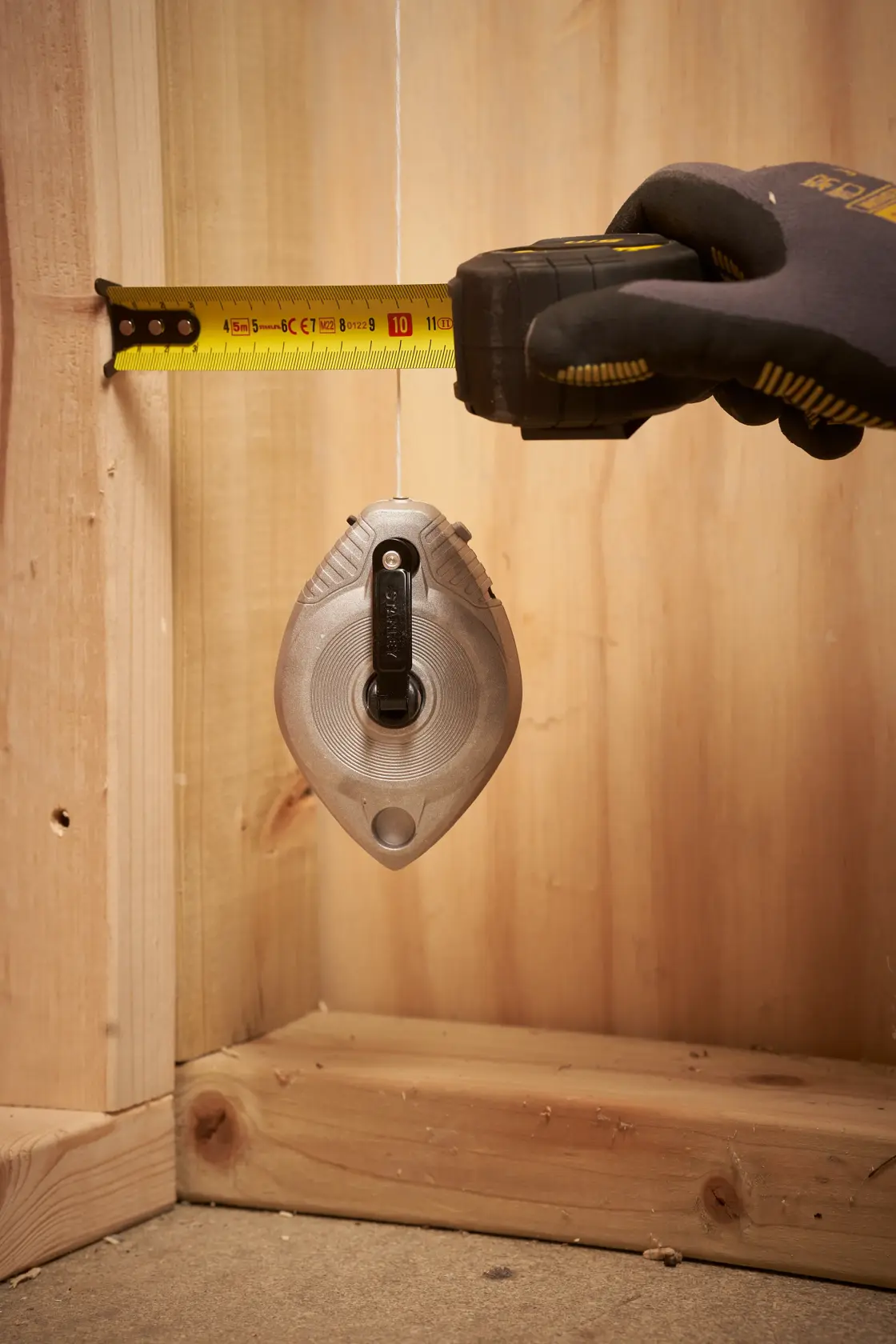 STANLEY 0-47-100 chalk line tool in use, hanging vertically with a hand measuring distance, construction setting.