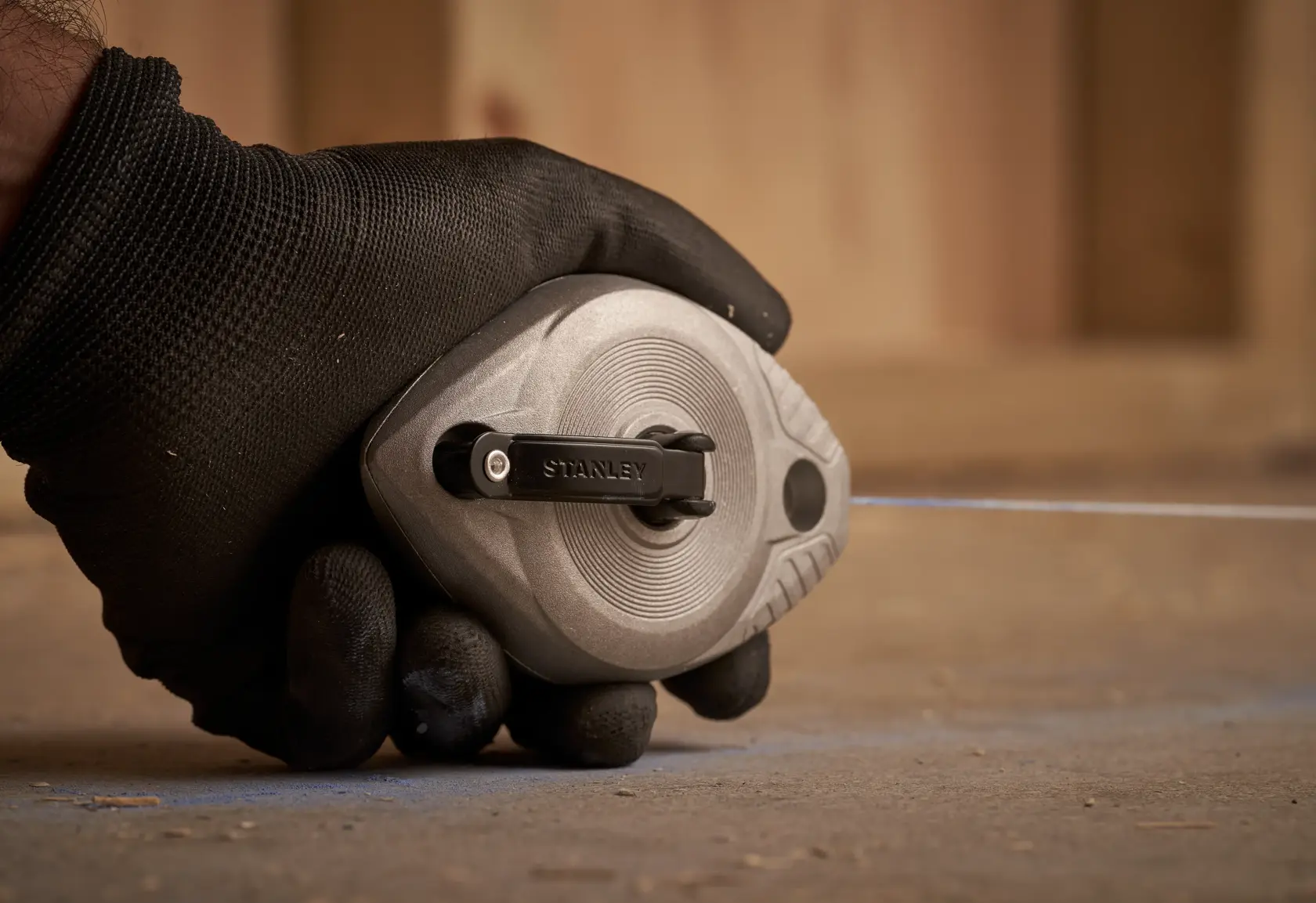 Photo of STANLEY 0-47-100 chalk line reel held in a gloved hand on a concrete surface.