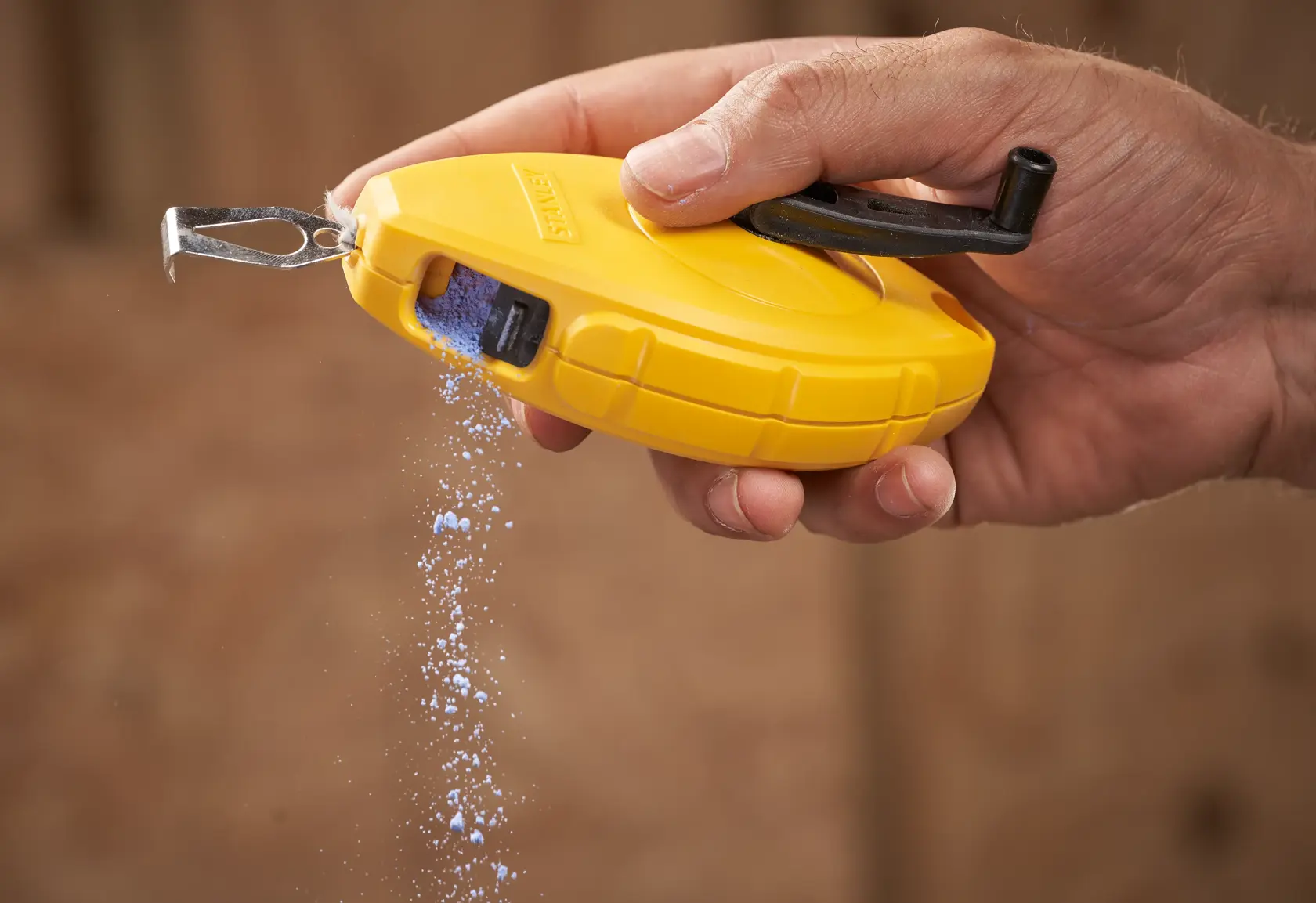 STANLEY 0-47-440 chalk line reel in yellow, hand-held with blue chalk pouring out, close-up photography.