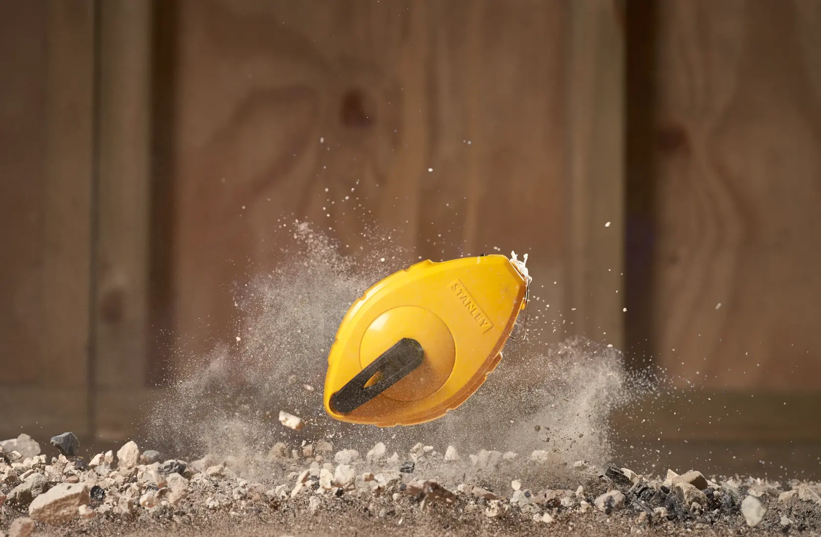 STANLEY 0-47-440 chalk line reel in yellow, dynamic action on dirt and rocks, photography product shot.