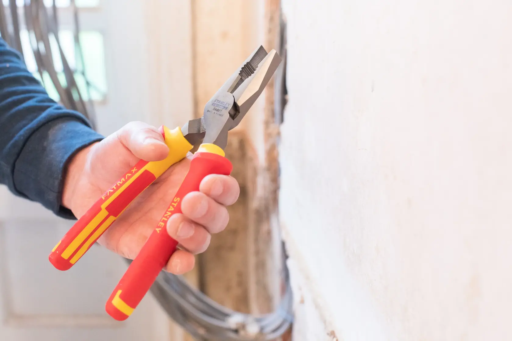 STANLEY 0-84-002 insulated pliers with red and yellow handles, held near a wall, product photography.