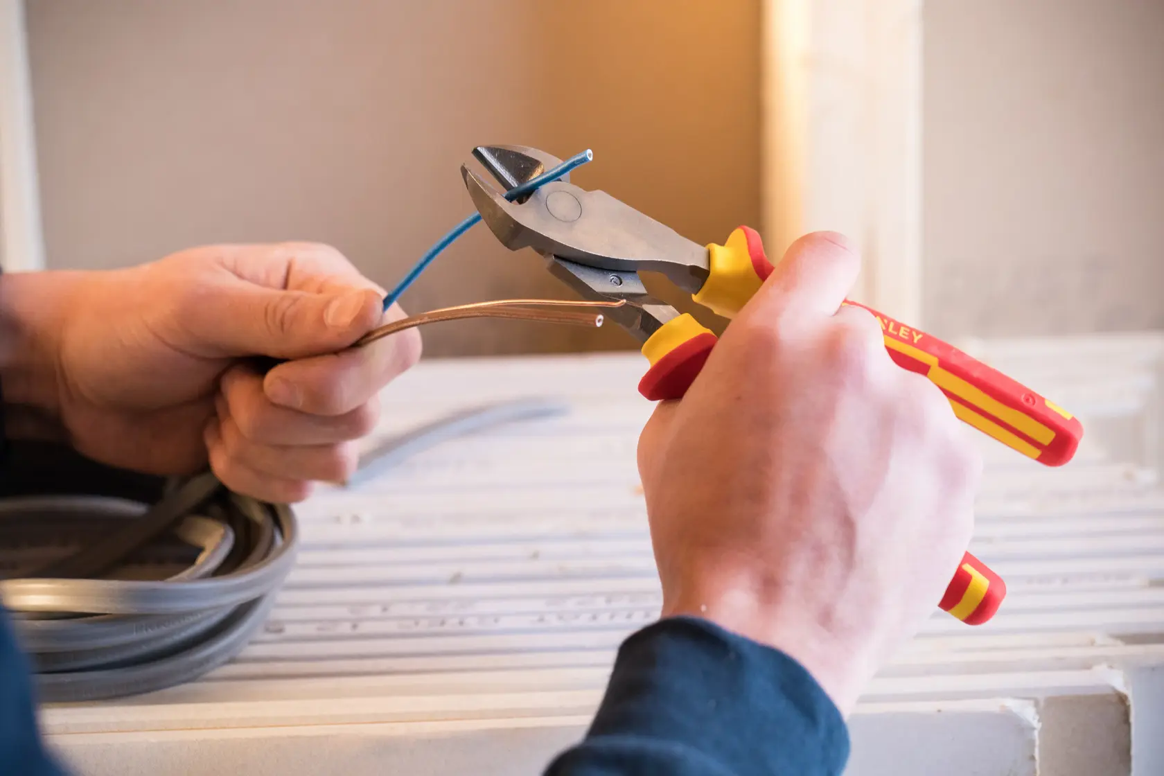 Stanley 0-84-004 insulated diagonal pliers cutting blue wire, close-up photo of hands in workshop.