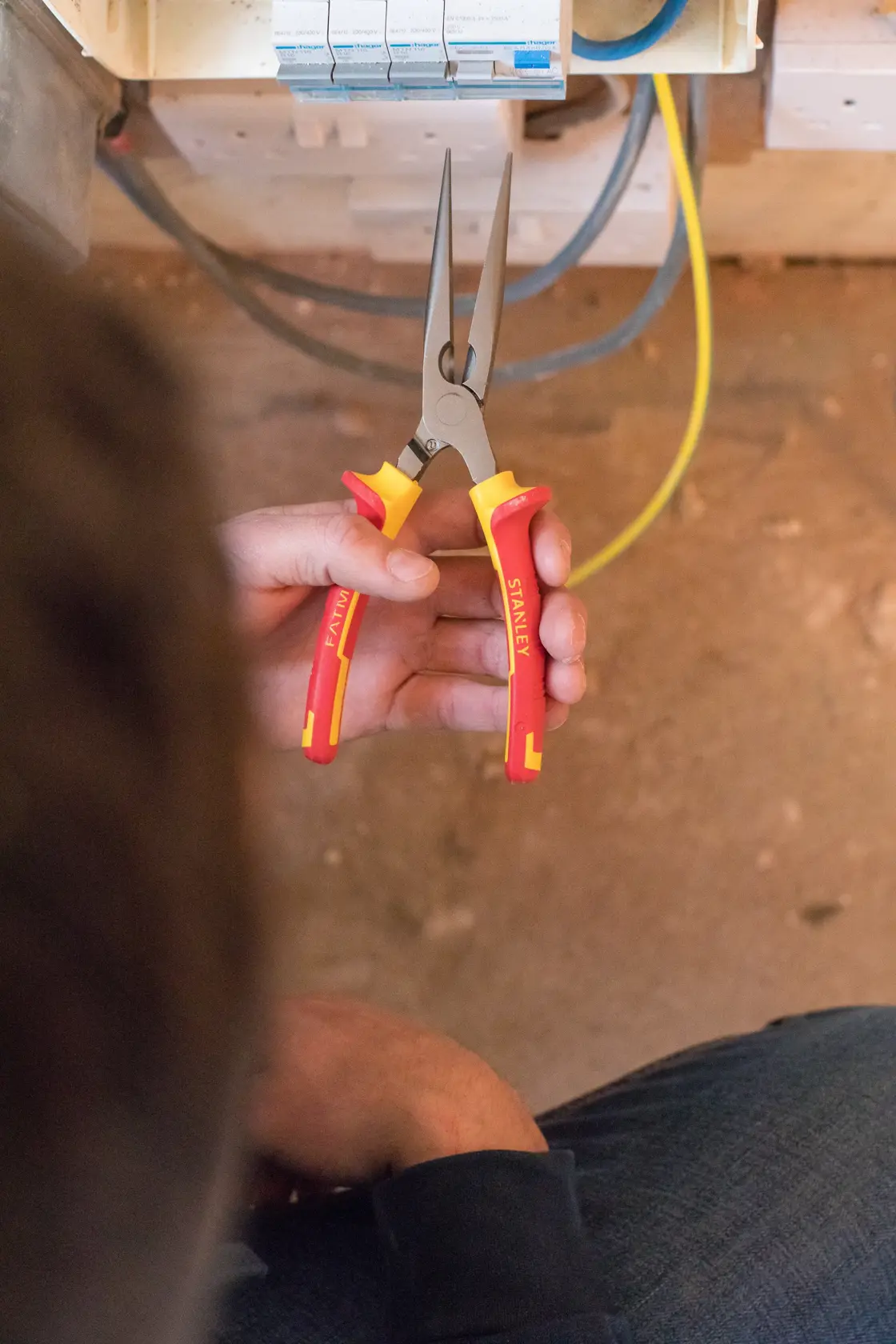 Photo of STANLEY 0-84-007 insulated long nose pliers with red and yellow handles in hand, electrical context.