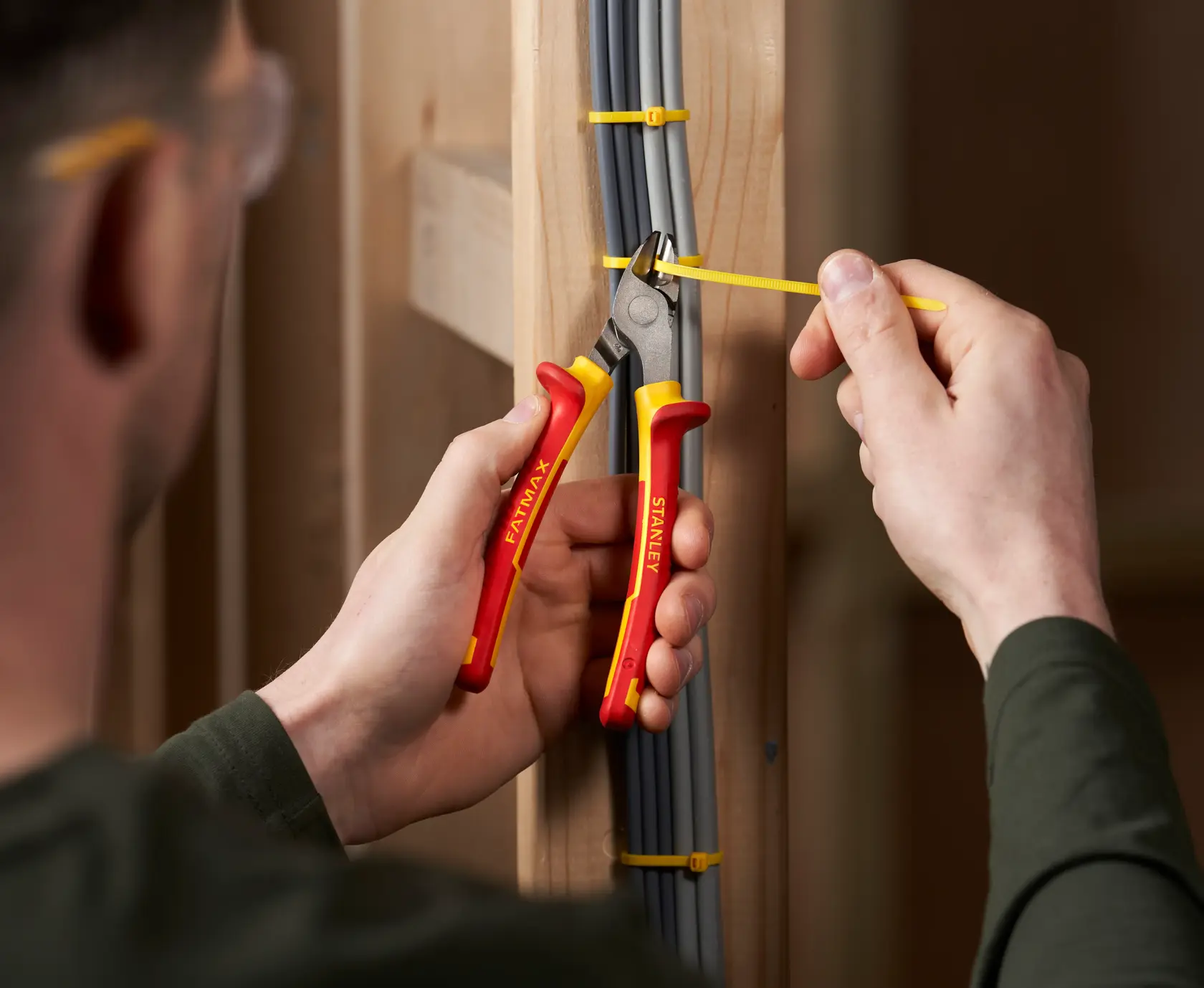 Photo of STANLEY 0-84-009 insulated side cutting pliers in use, cutting a yellow cable tie on electrical wires.