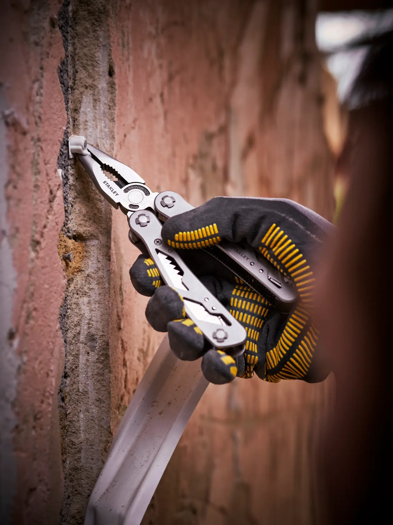 STANLEY 0-84-519 multi-tool pliers used on a brick wall, close-up photography of gloved hand.