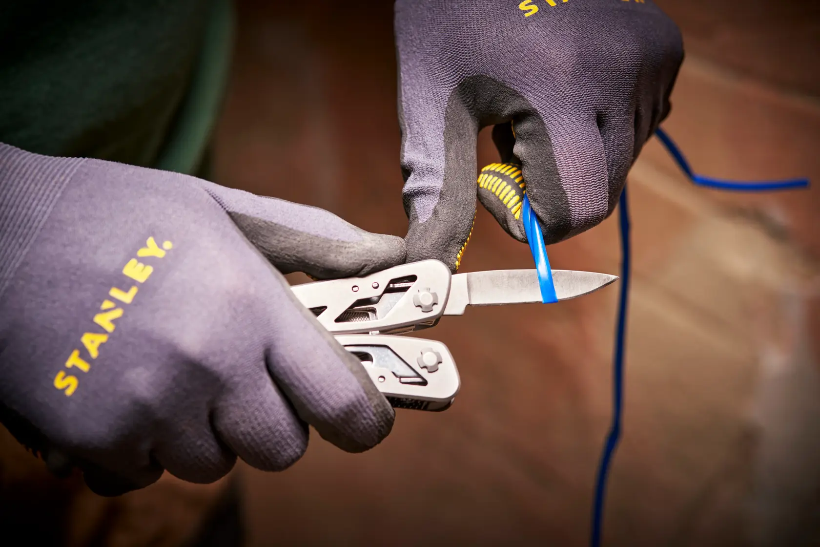 STANLEY 0-84-519 multitool blade cutting blue wire, close-up, worn with STANLEY gloves.