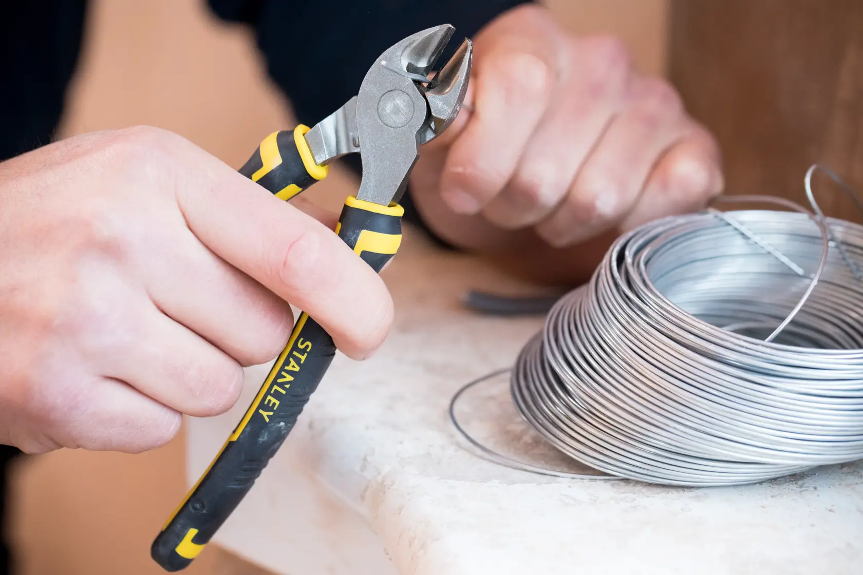 STANLEY 0-89-858 wire cutter pliers used to cut silver wire, close-up with coil on table.