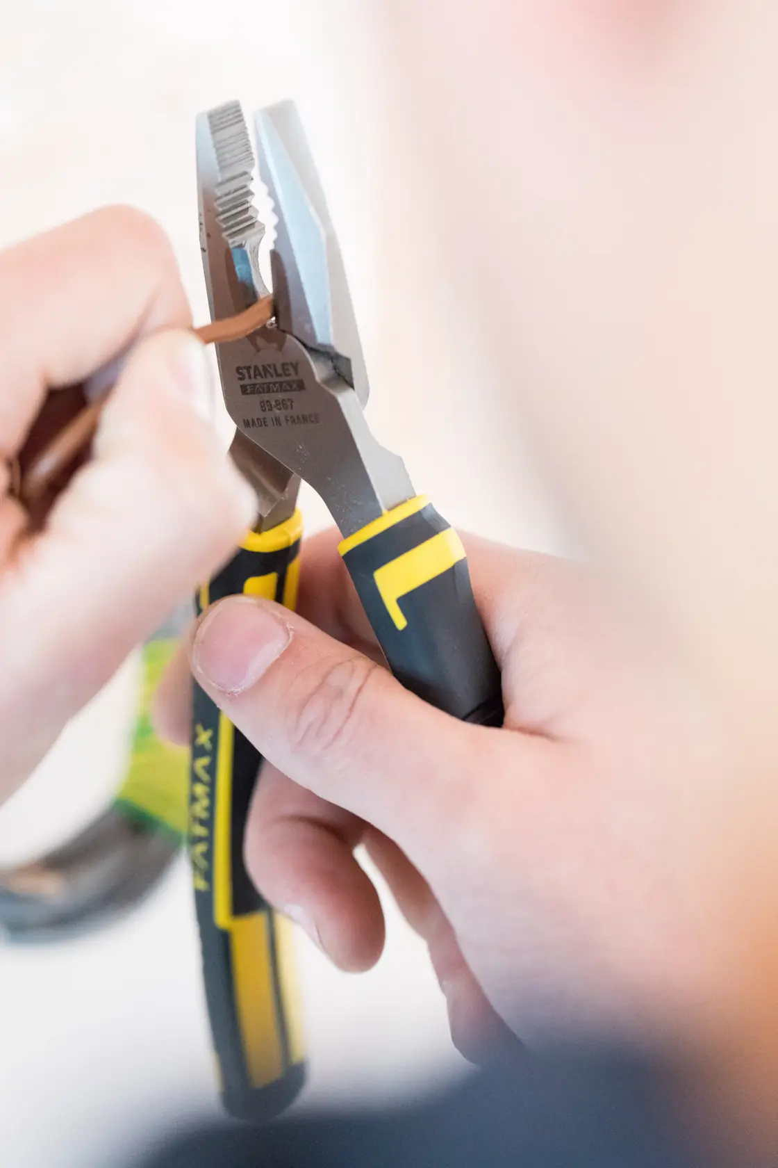 Photo of STANLEY 0-89-867 pliers with yellow and black grips being used to grip a brown wire.