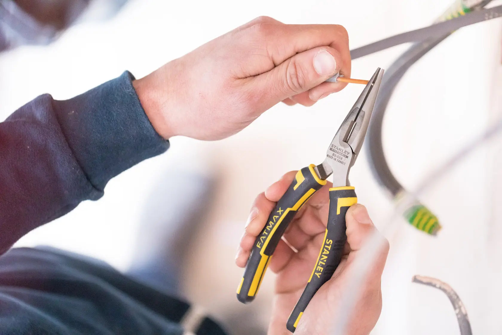 STANLEY 0-89-869 long nose pliers with yellow and black handle in use by hand, close-up photo.