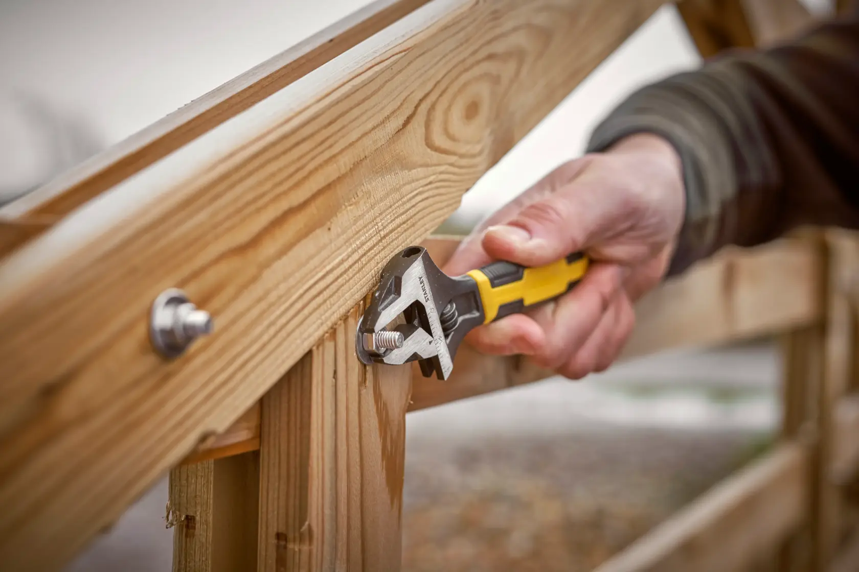 STANLEY 0-90-947 adjustable wrench in use tightening a bolt on a wooden fence.