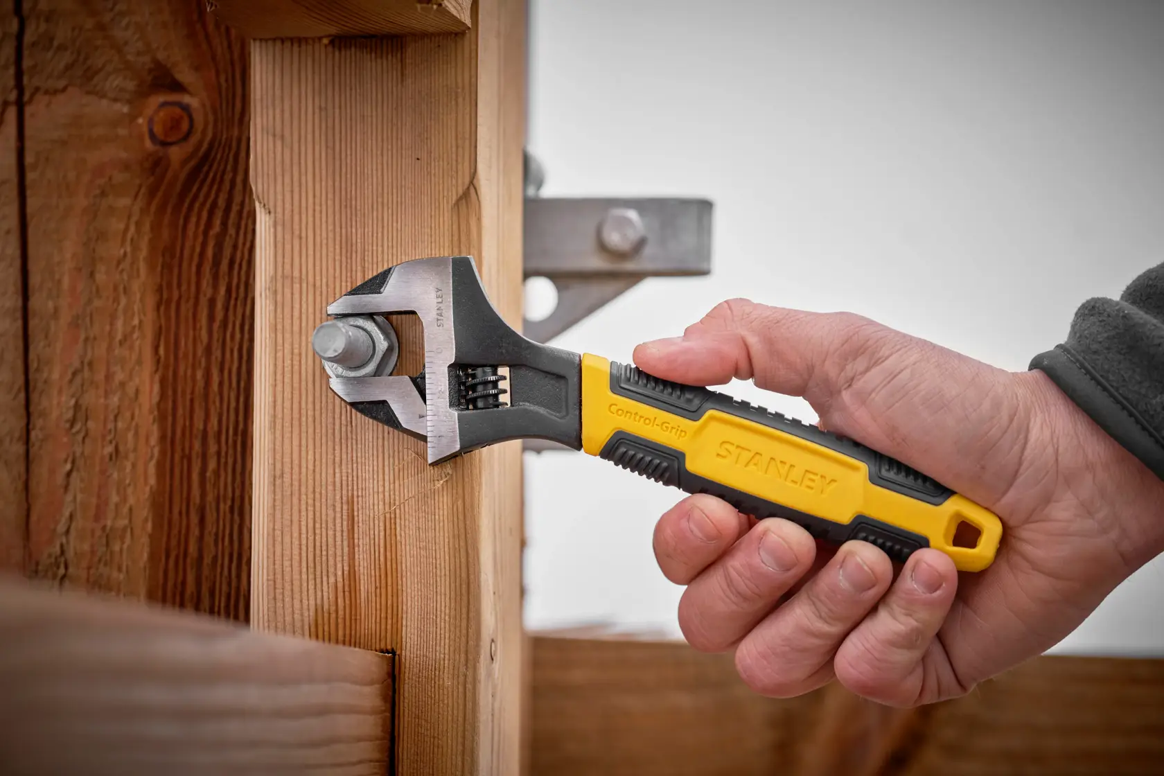 STANLEY 0-90-949 adjustable wrench with yellow and black handle used on a bolt attached to wooden beams.
