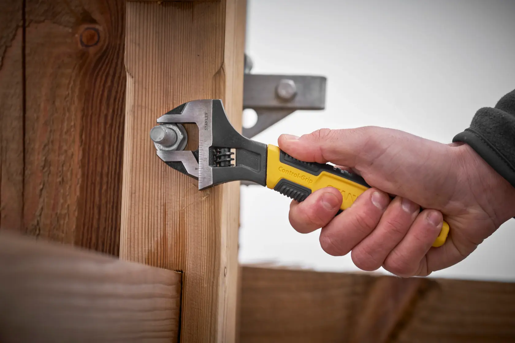 Stanley 0-90-949 adjustable wrench with yellow handle tightening bolt on wooden structure, side angle.