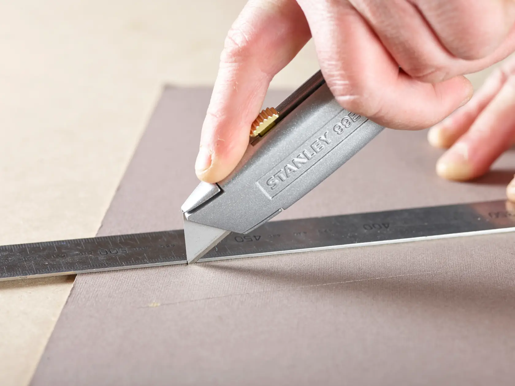 Photo of STANLEY 1-11-911 utility knife cutting material with a metal ruler for alignment.