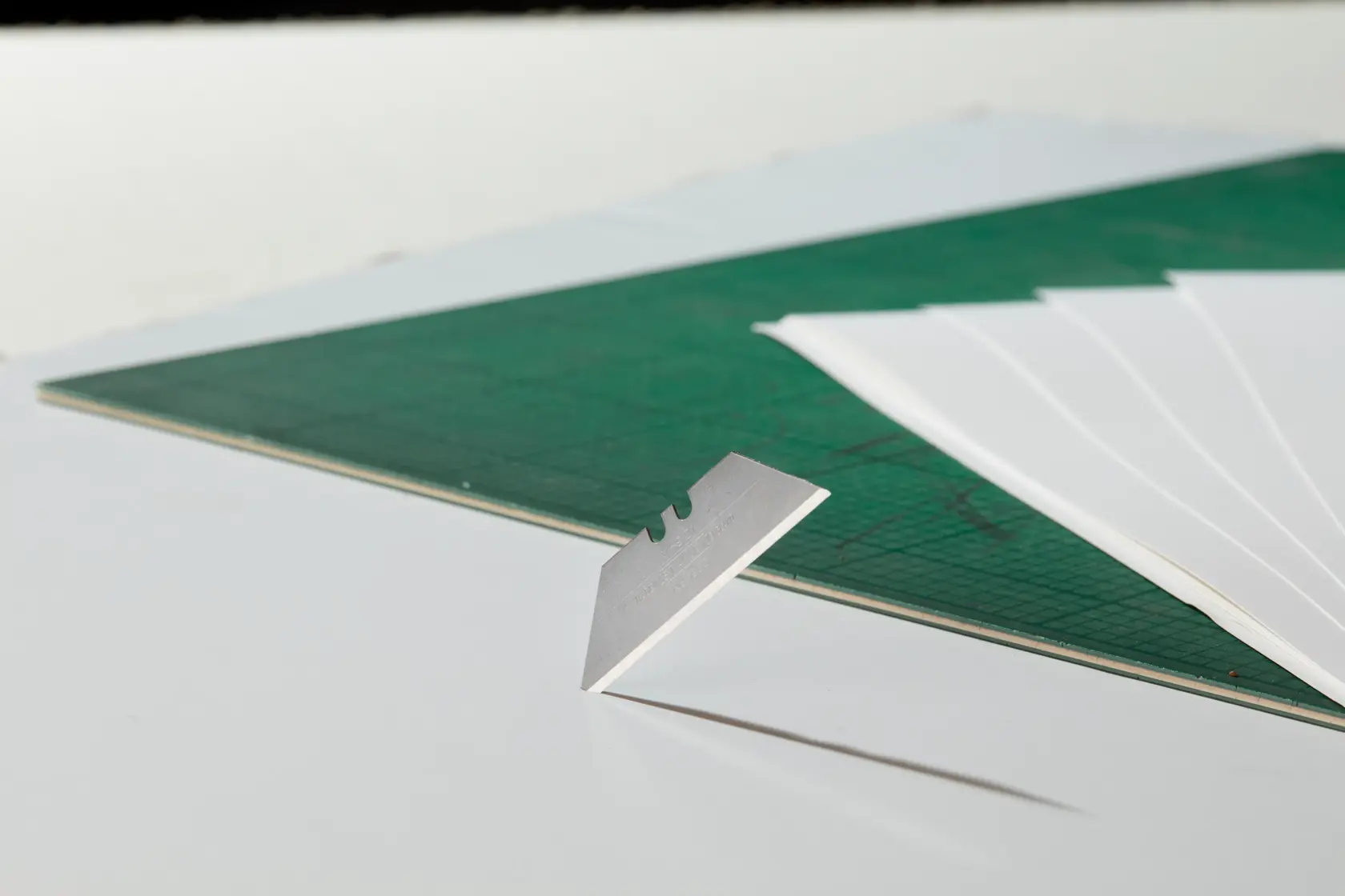 STANLEY 1-11-921 utility blade standing upright near green cutting mat and white paper sheets, side angle.
