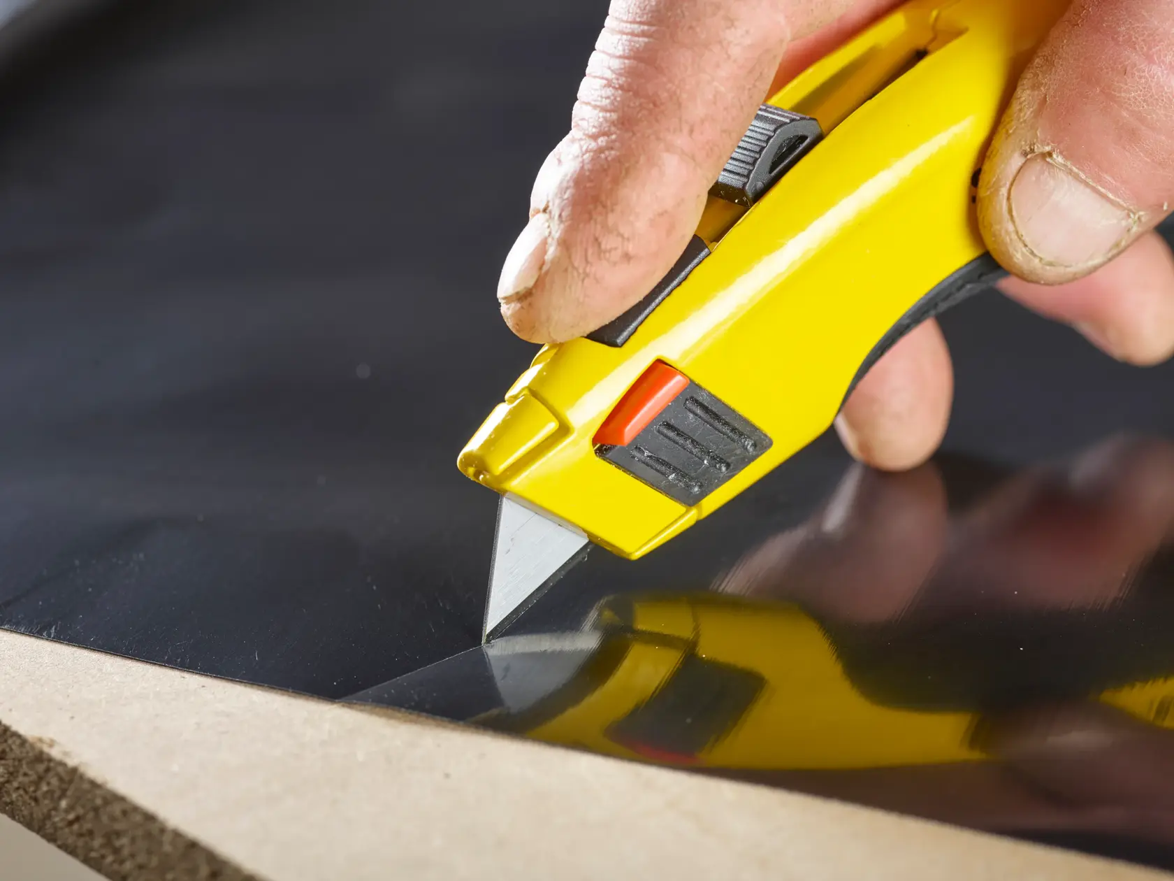 STANLEY 1-11-921 utility knife cutting black material, close-up photography of yellow handle and blade in use.