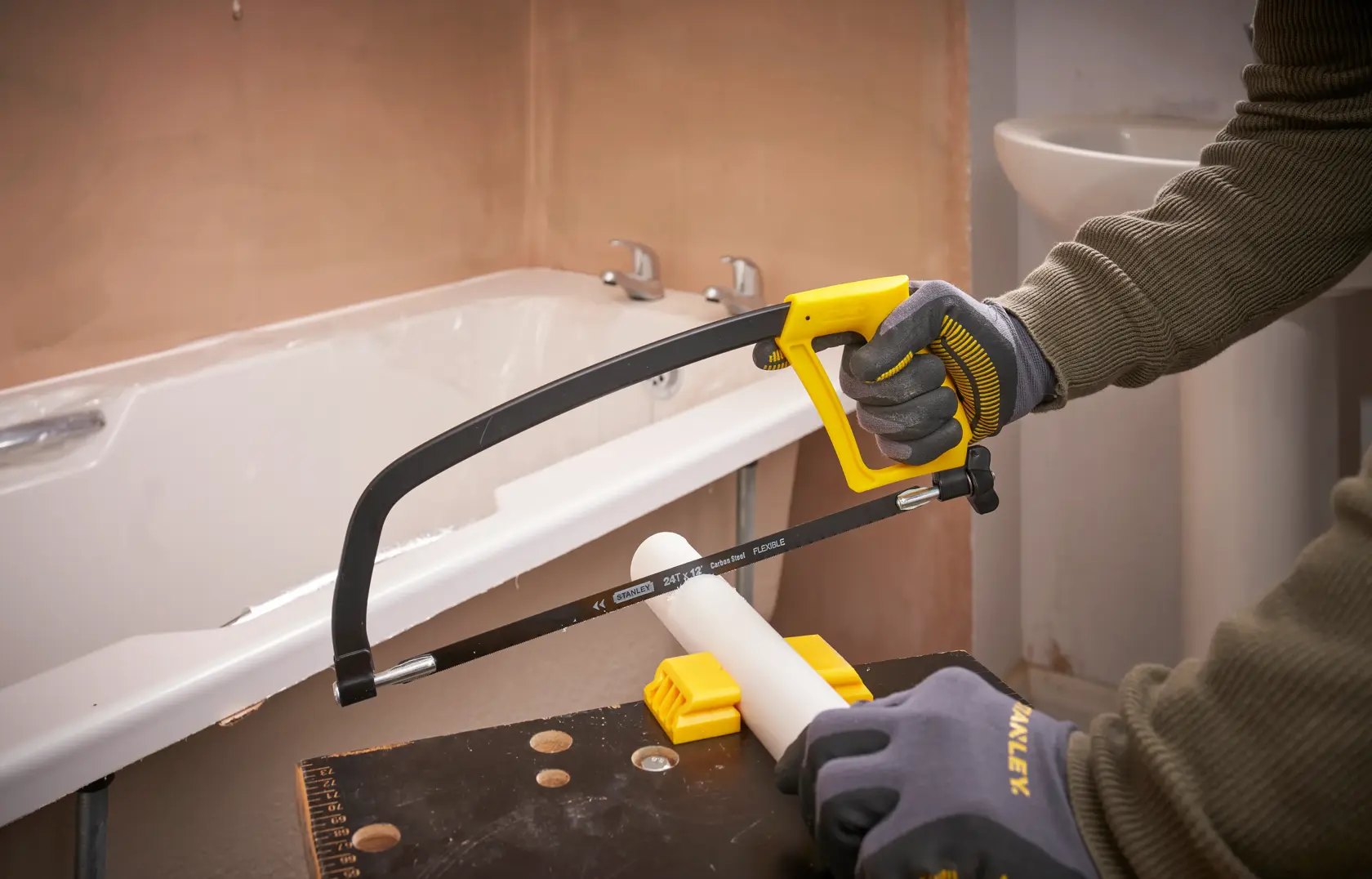 STANLEY 1-15-122 hacksaw cutting white PVC pipe in bathroom, close-up action shot.