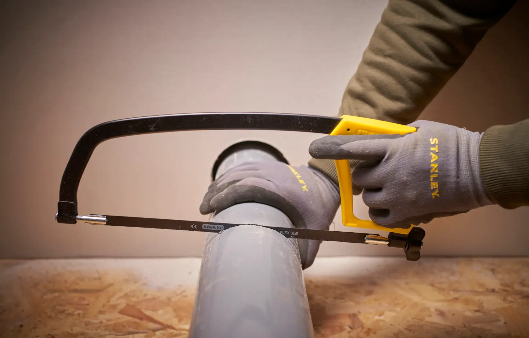 STANLEY 1-15-122 hacksaw with yellow handle cutting grey pipe, close-up angle, product photography.
