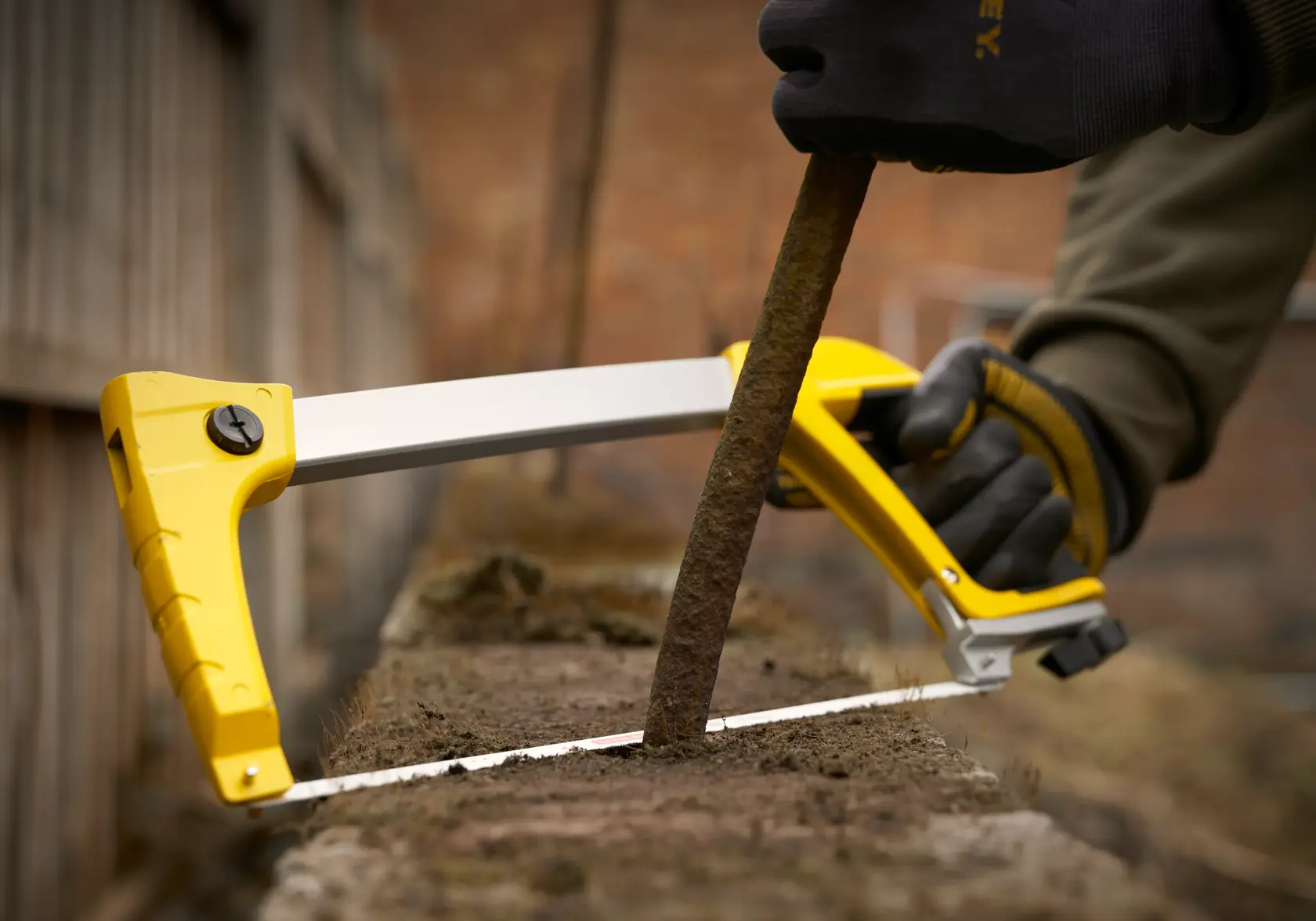 STANLEY 1-20-110 saw in use, cutting a rusty metal rod outdoors, close-up of yellow frame and hand in gloves.