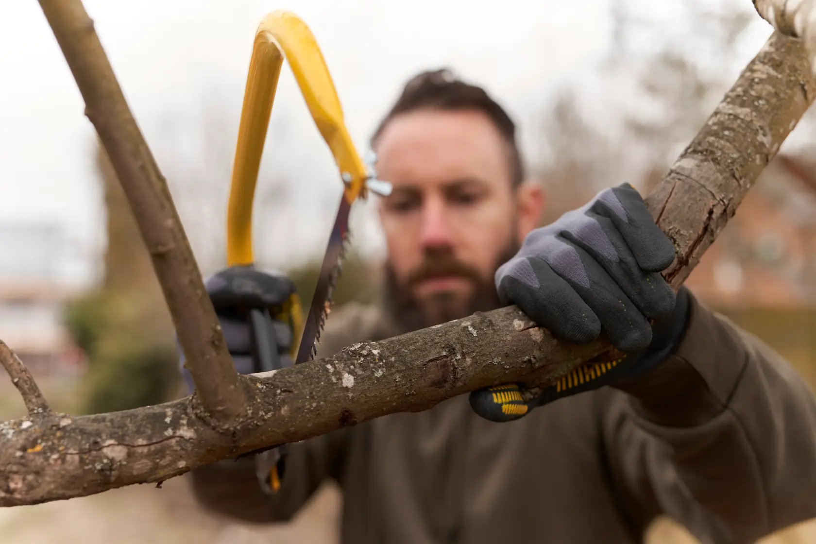 STANLEY 1-20-447 hand saw with yellow frame cutting tree branch outdoors, person wearing work gloves.