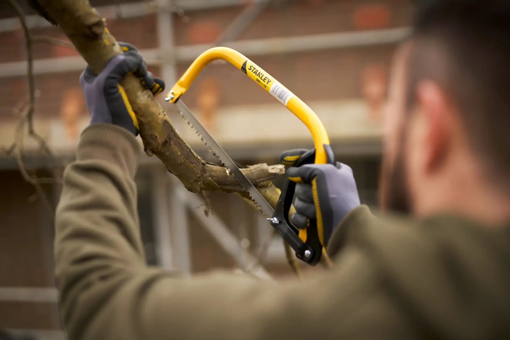 Stanley 1-20-447 bow saw cutting tree branch, yellow frame, outdoor setting.