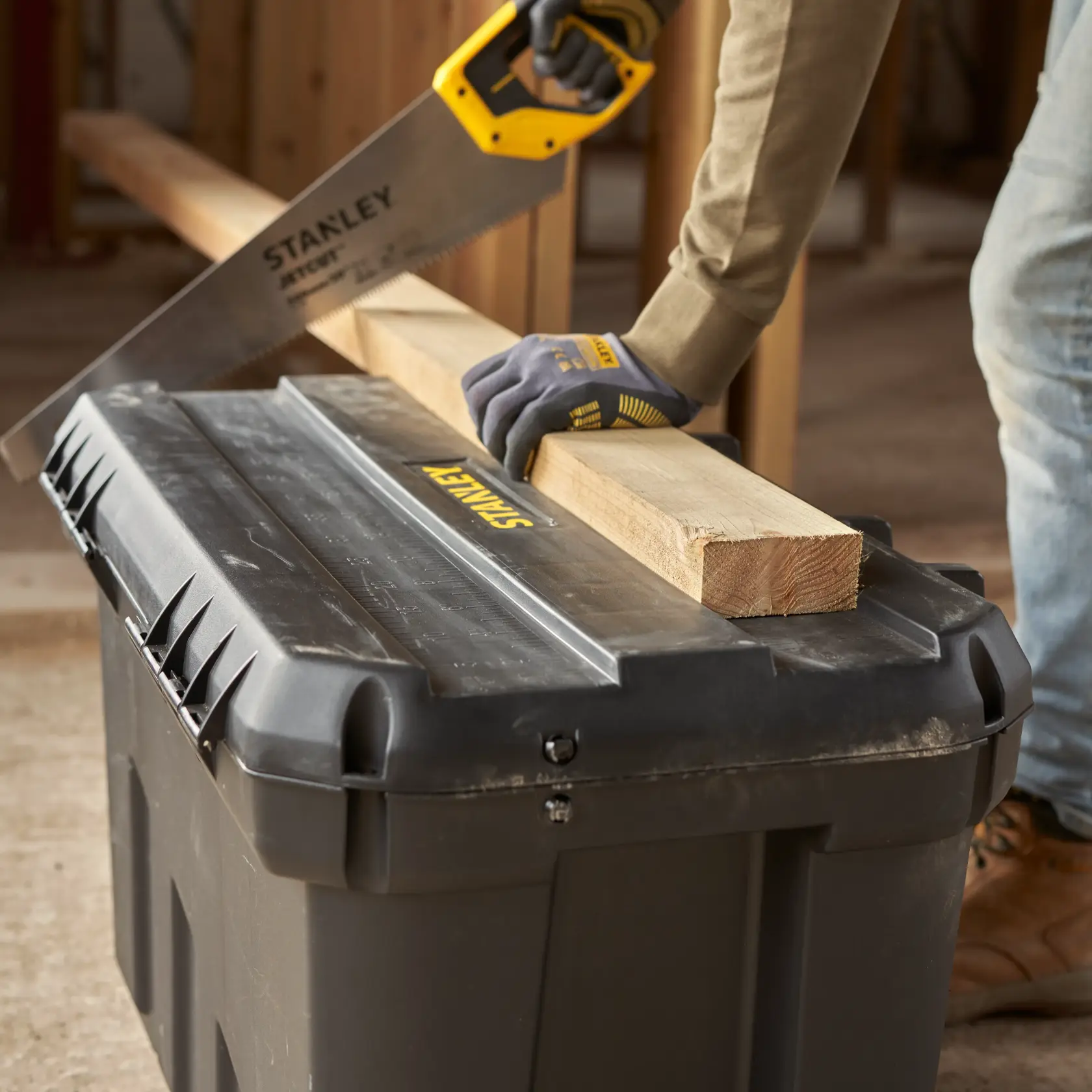 STANLEY 1-92-978 black tool box used as sawing platform with wood and hand saw in workshop setting.