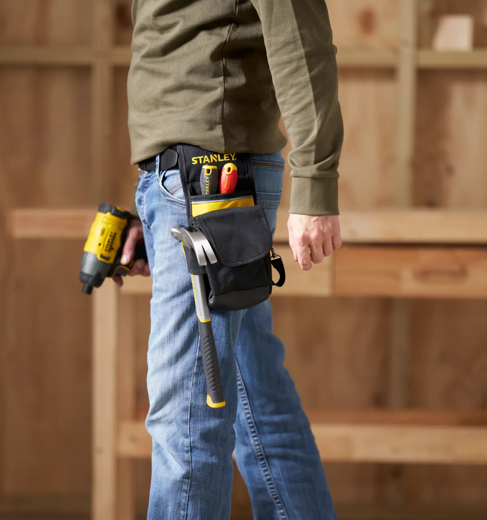 STANLEY 1-93-329 tool pouch with hammer, screwdrivers, and utility knife attached to a belt, side angle, workshop background.