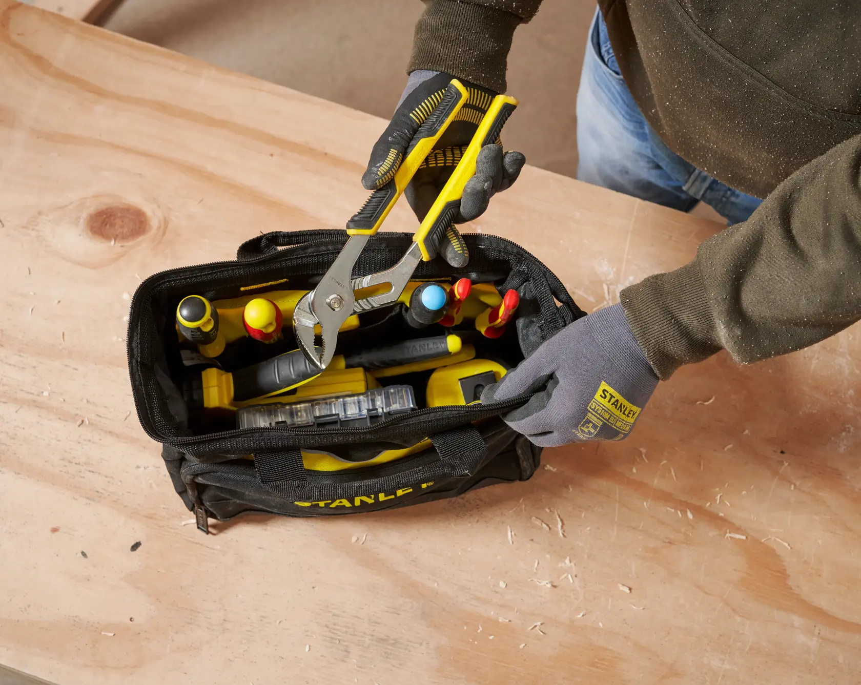 STANLEY 1-93-330 tool bag with yellow-handled pliers on wooden table, photography top view.