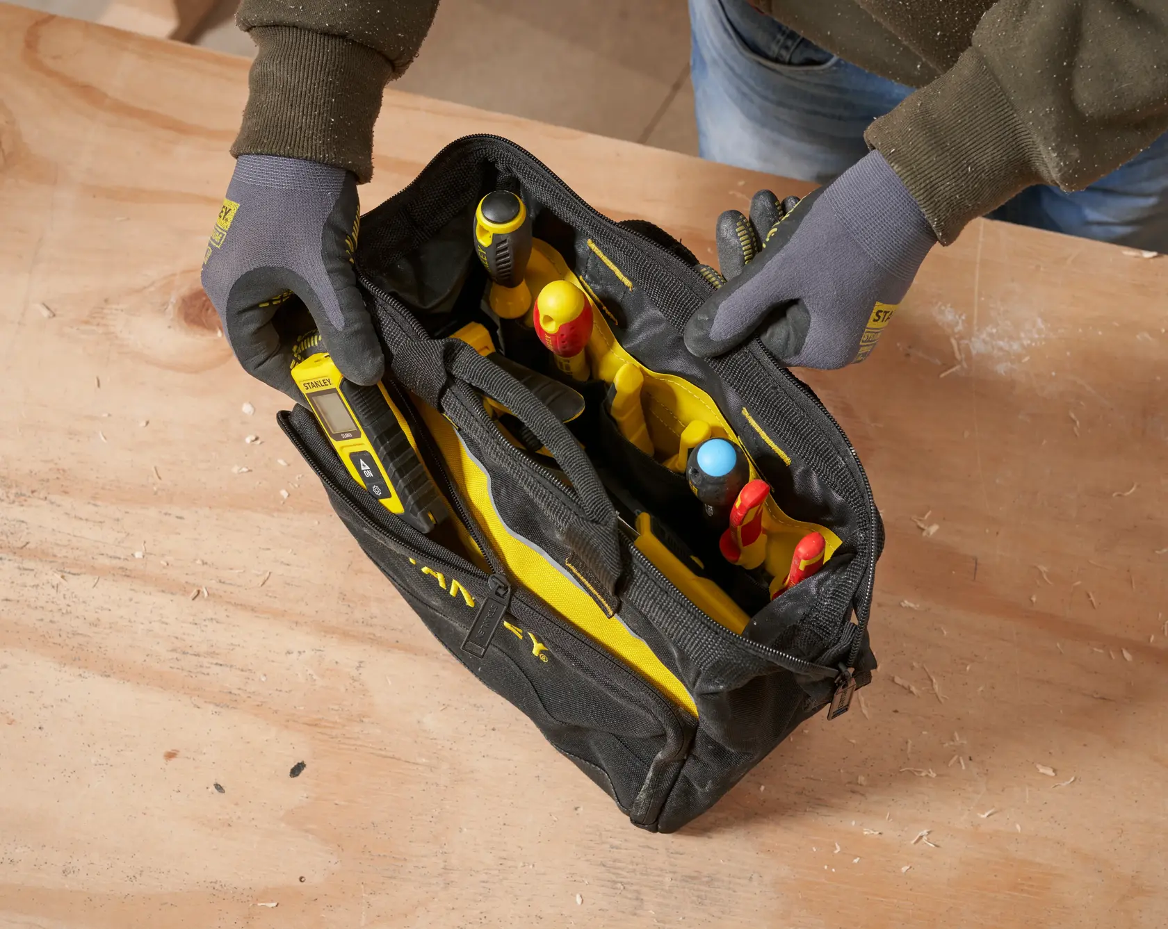 STANLEY 1-93-330 tool bag filled with assorted hand tools, top view, on wooden surface.