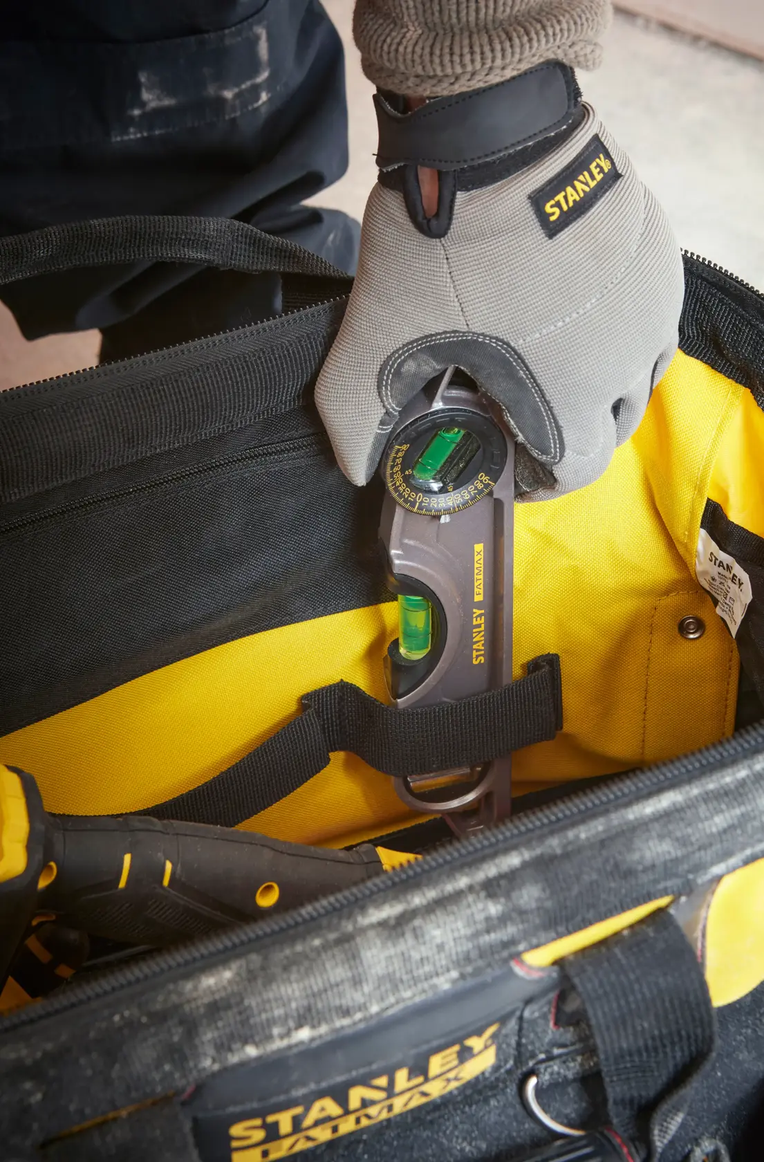 Photo of STANLEY 1-93-950 tool bag with worker placing digital angle gauge inside, close-up top view.