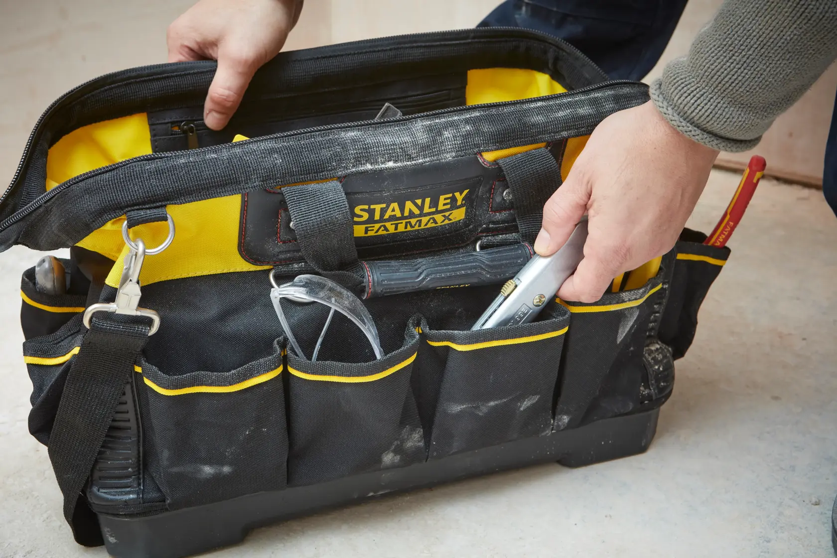 STANLEY 1-93-950 tool bag with yellow and black design, open with hand, tools and safety glasses visible.