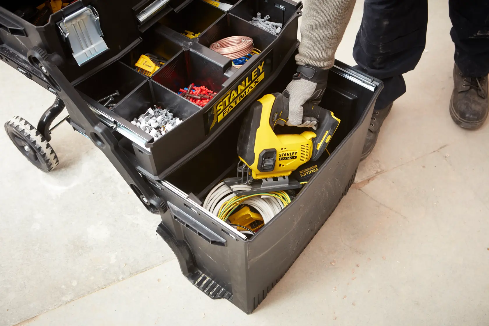 STANLEY 1-94-210 tool organizer with compartments, worker accessing lower bin with power tool and cables.
