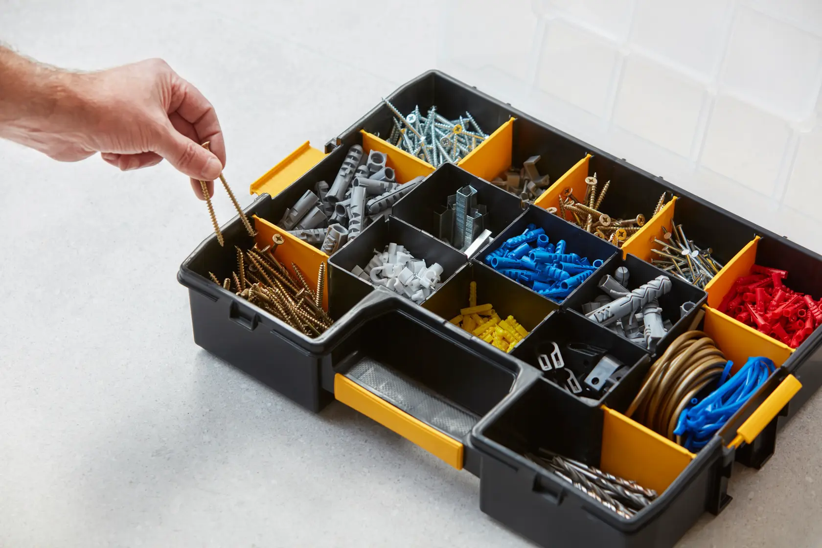 STANLEY 1-94-745 organizer box with compartments holding screws, wall plugs, and hardware, person picking screws.