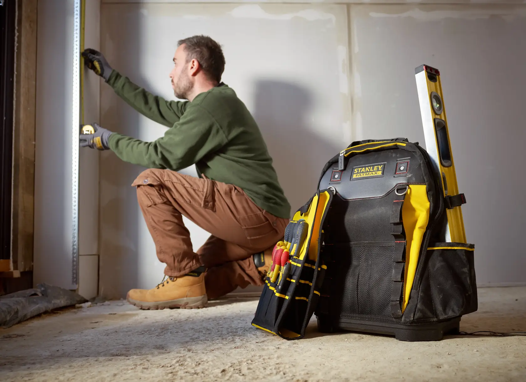 STANLEY 1-95-611 tool backpack with tools and level, shown upright on floor at construction site.